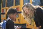 photo of Amy Schott greeting a student with school buses in the background